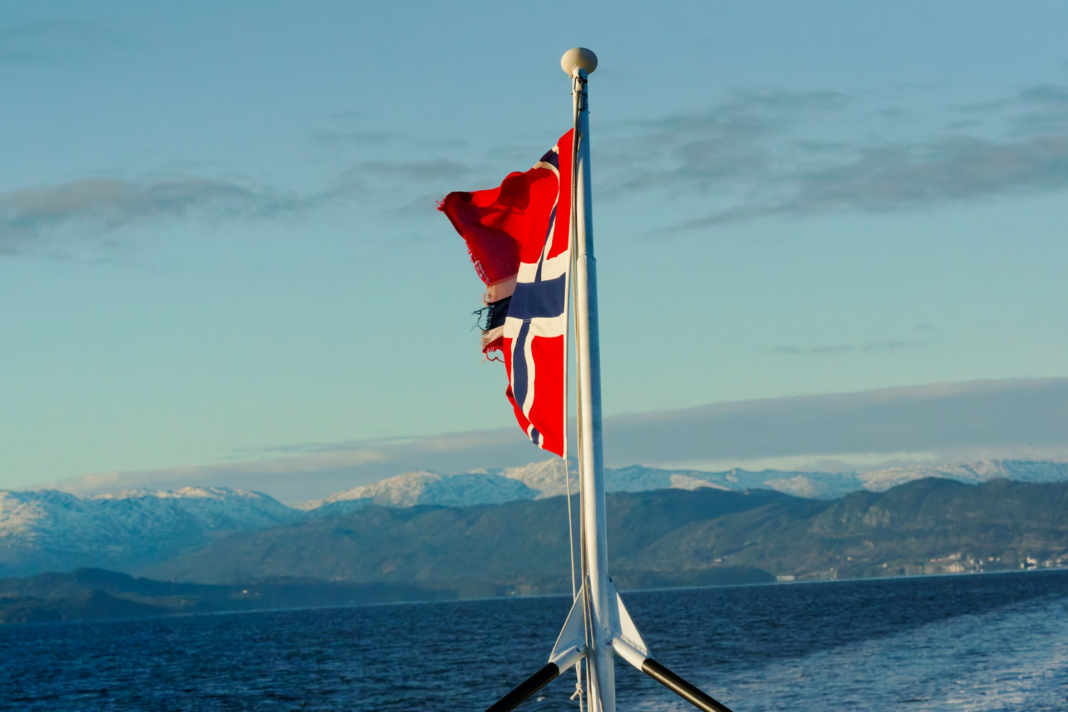 norwegian flag waving on a pole over the ocean